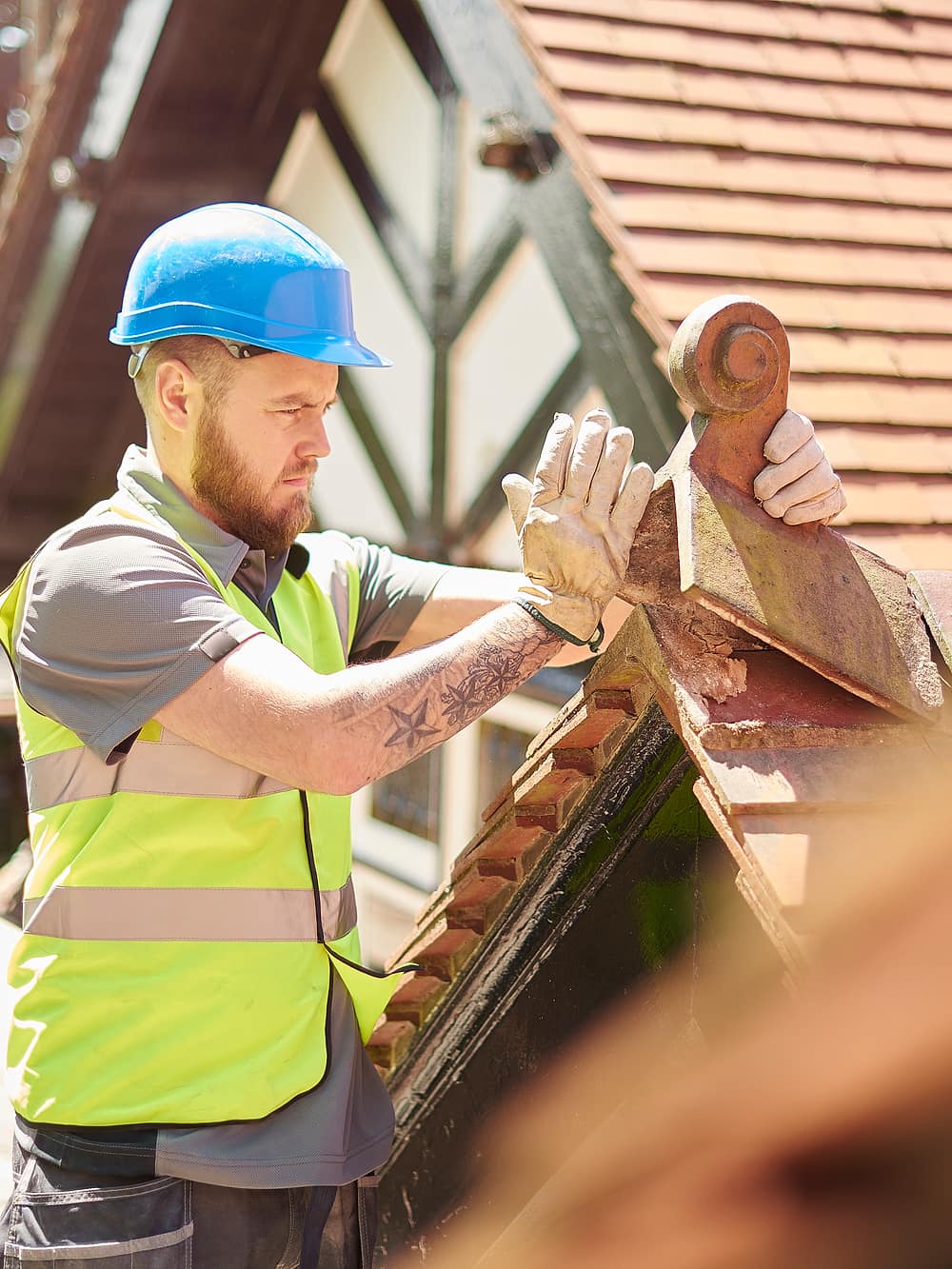 A roofer fitting a clay finial on a scaffolded roof