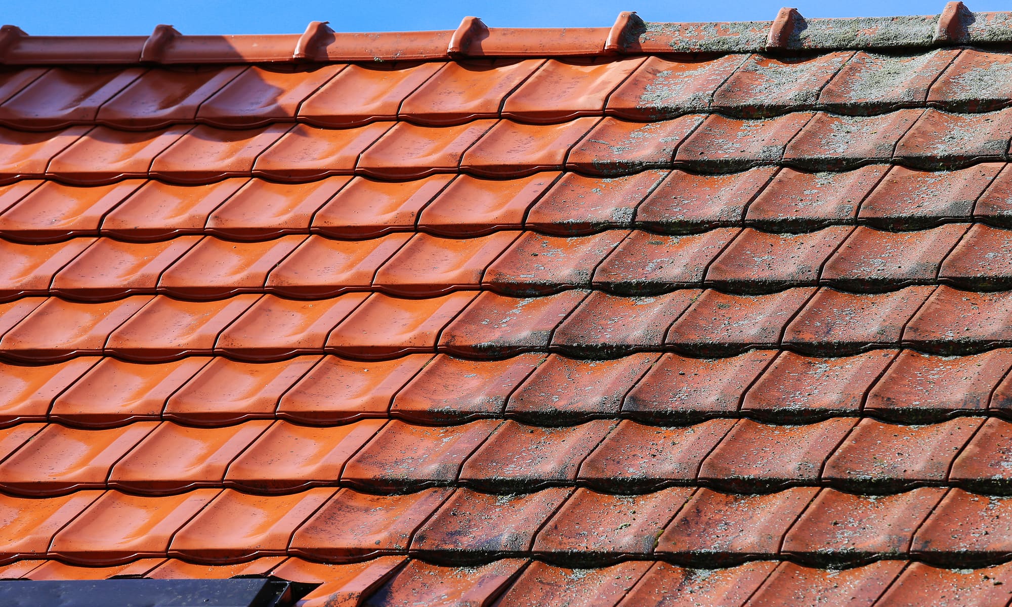 New clay tiles laid beside weathered, lichen-covered tiles on the same roof