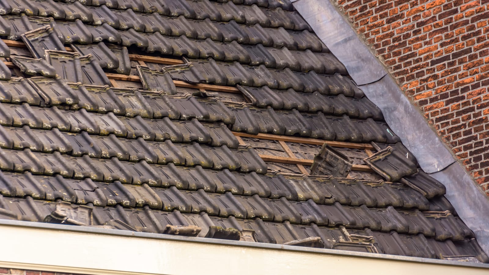 Slipped and displaced pantiles on a roof slope beside brickwork